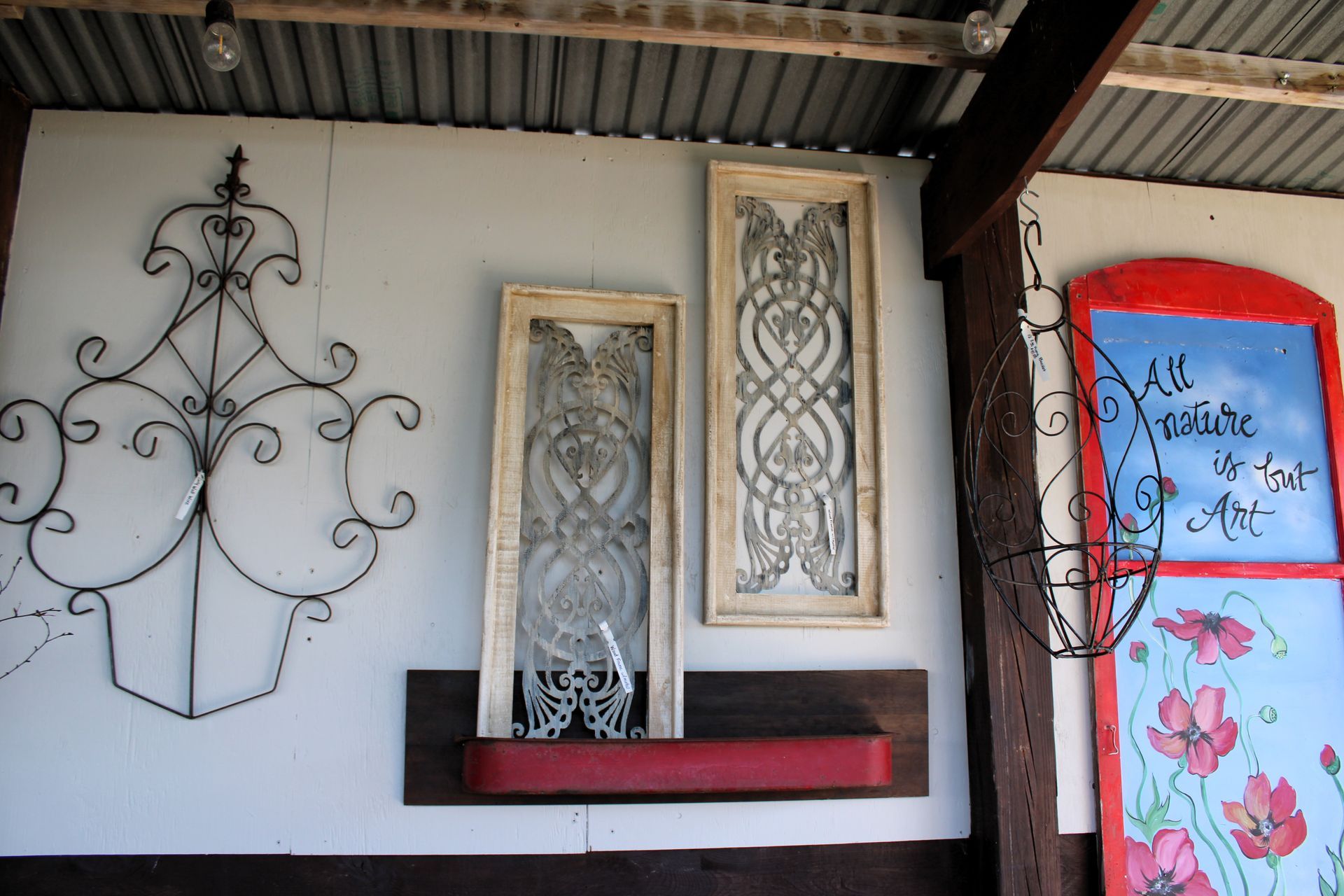 Wall decor: wrought iron designs and framed art on a white wall; red flower box; red and blue painted door.