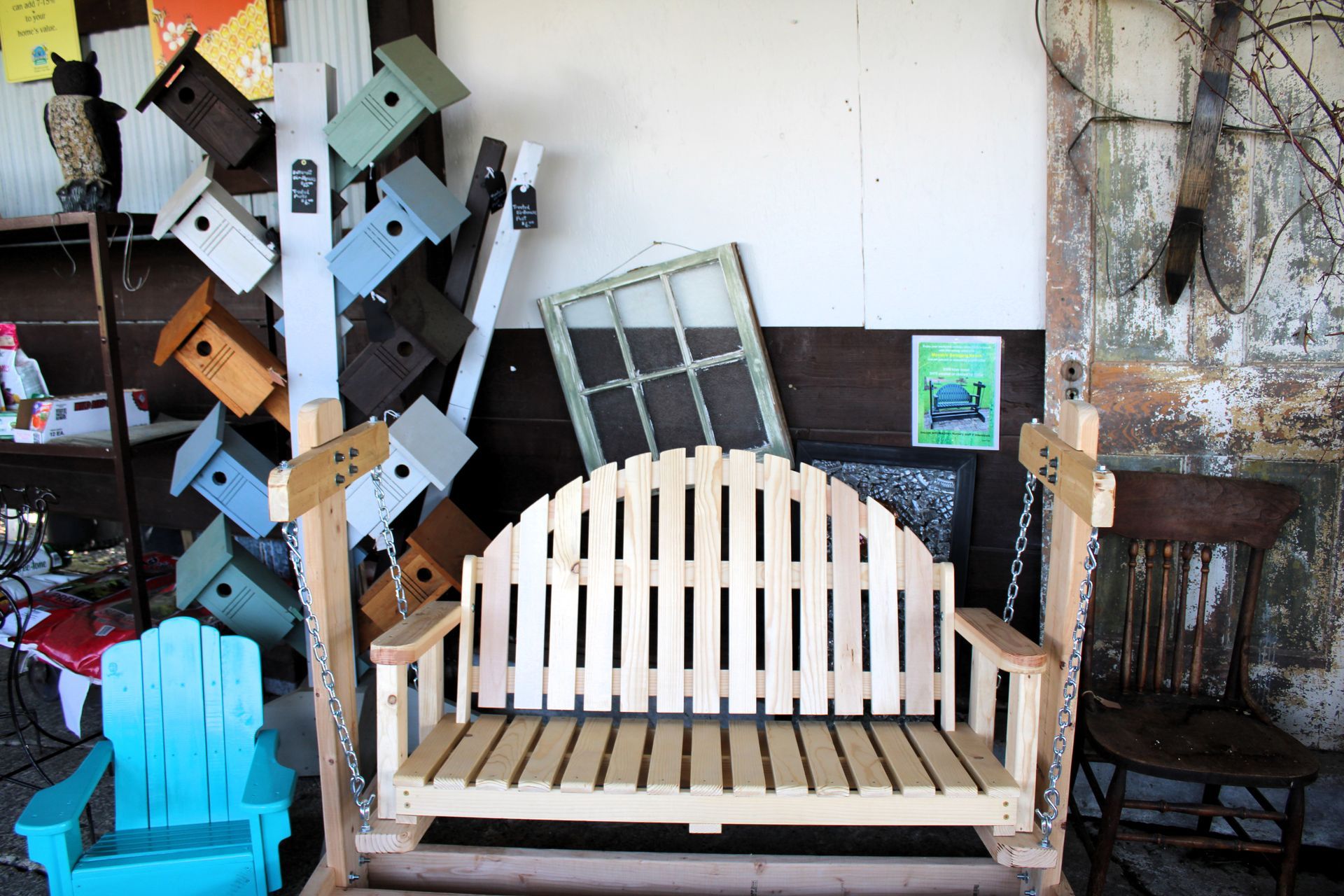 Wooden swing bench and blue chair by a wall with birdhouses and a window.