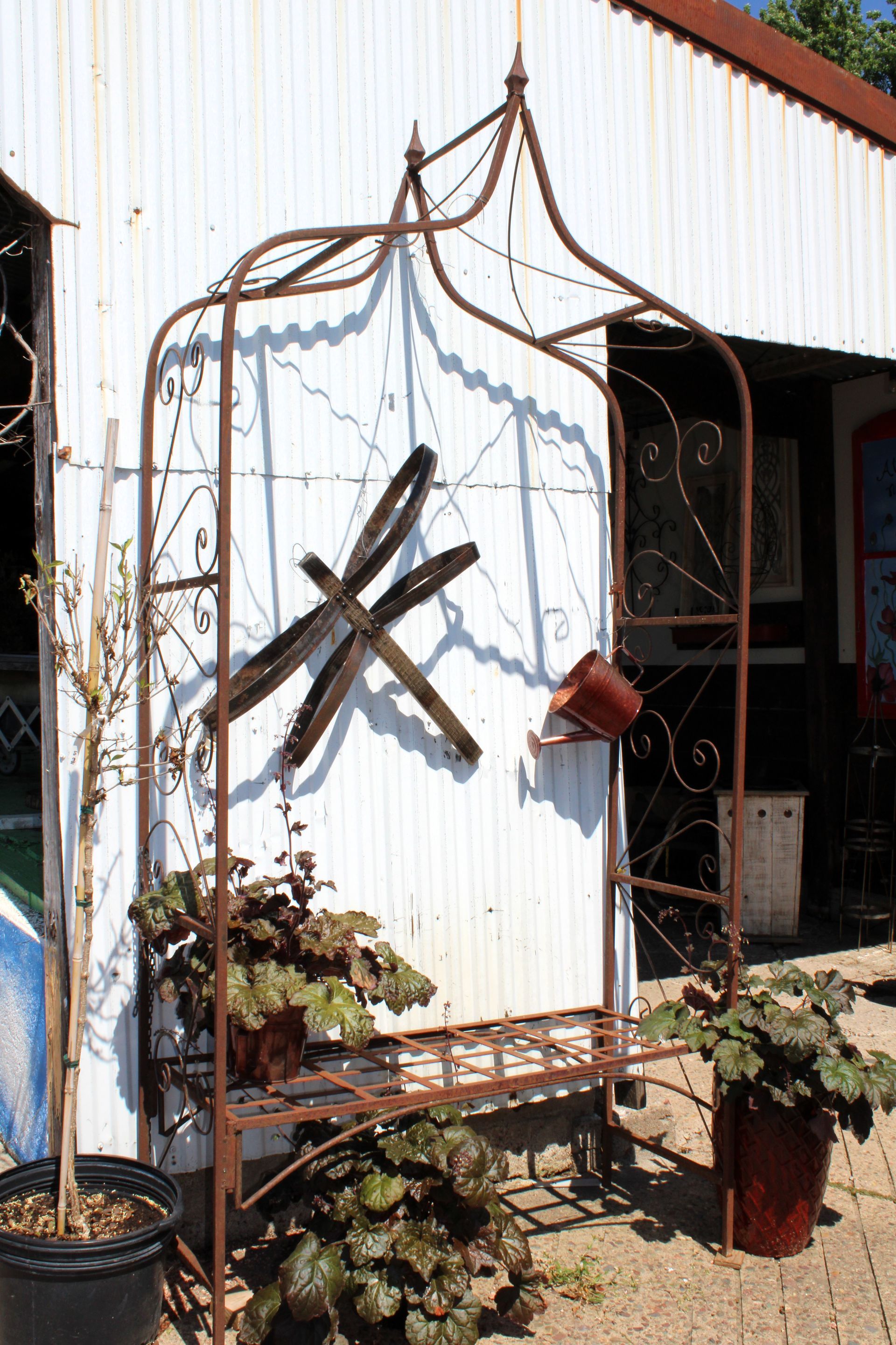 Wrought-iron garden bench with dragonfly decoration, potted plants in front of a white building.