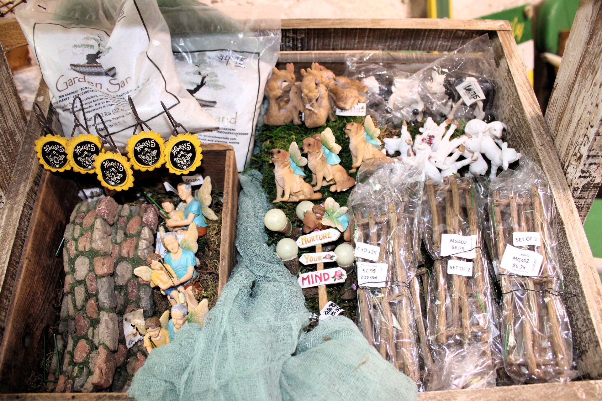 Display of various decorative items in wooden bins, including figurines, sticks, and signs.