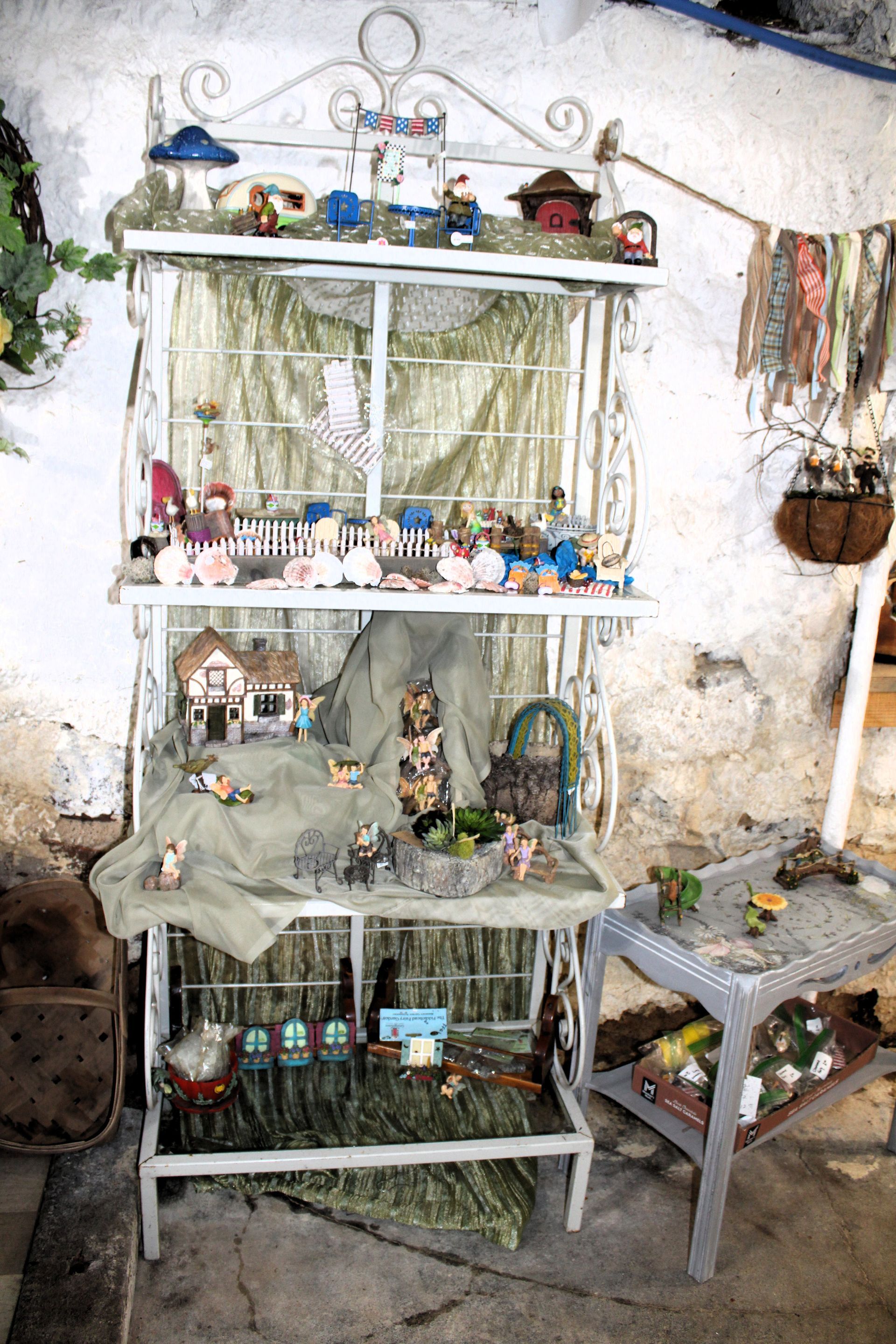 White wire shelving unit displays miniature figurines and houses with a textured wall backdrop.