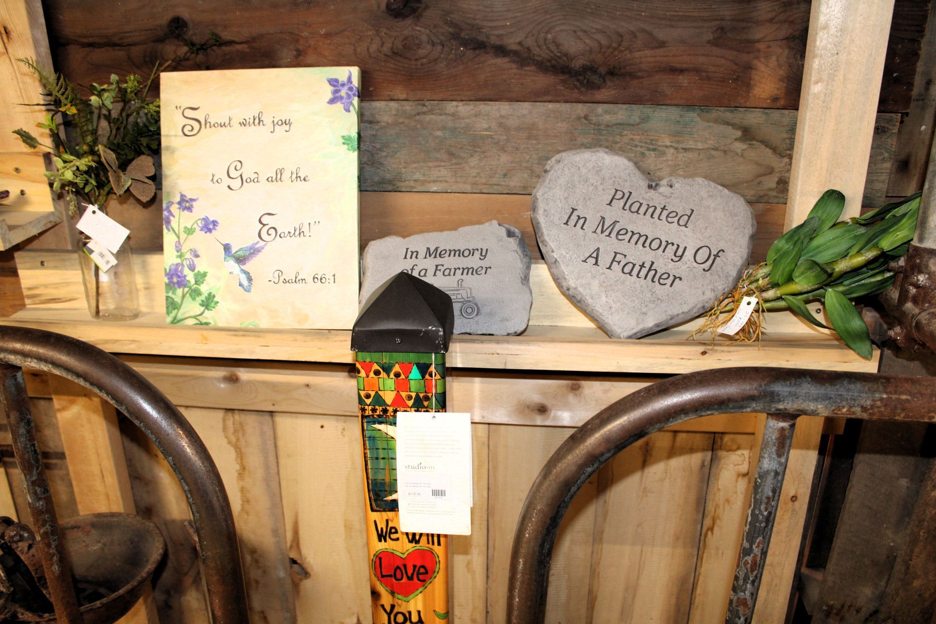 Shelf display with heart-shaped stone, memorial sign, and artwork with script on rustic wooden background.