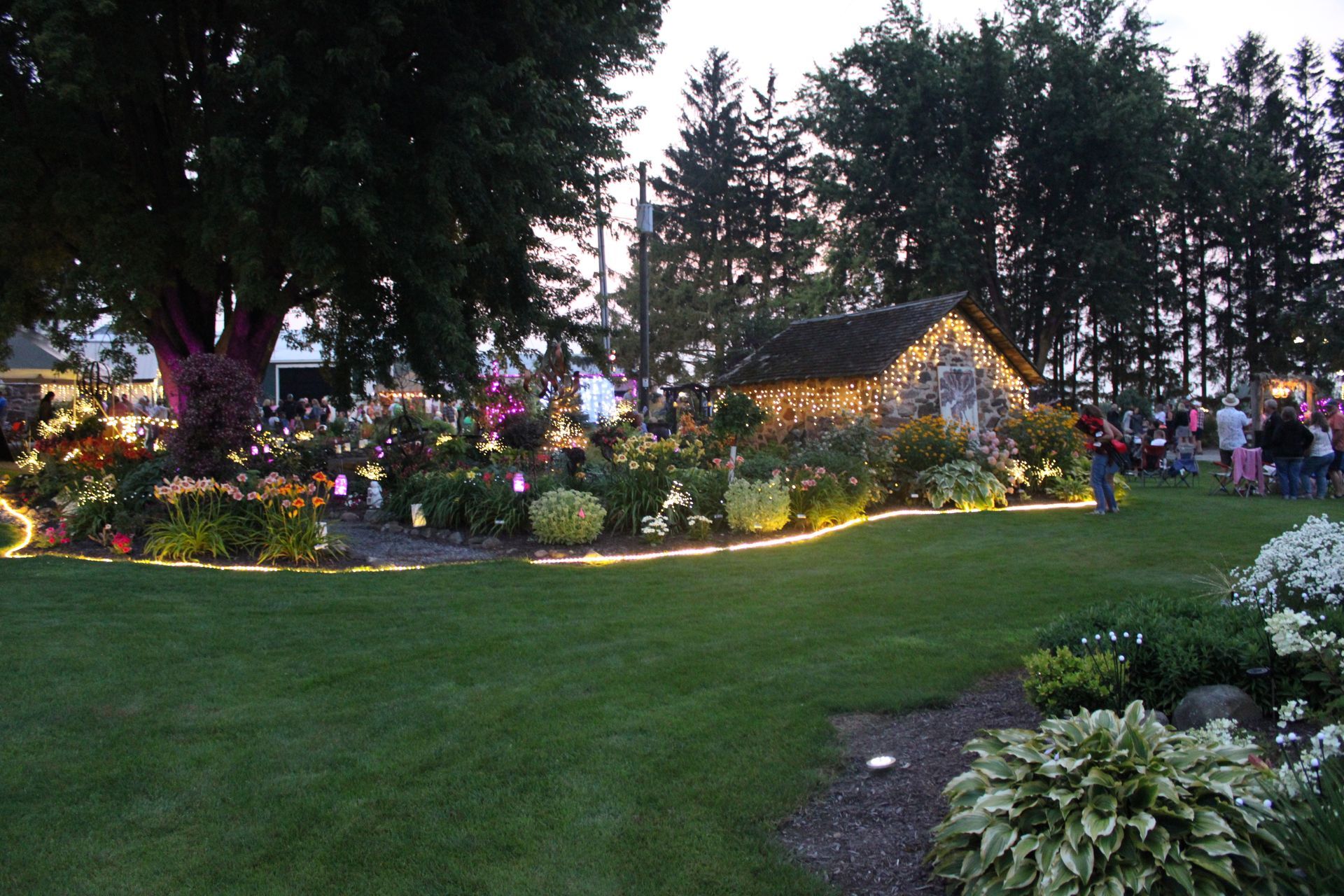Garden with illuminated flowers and small building, evening scene.