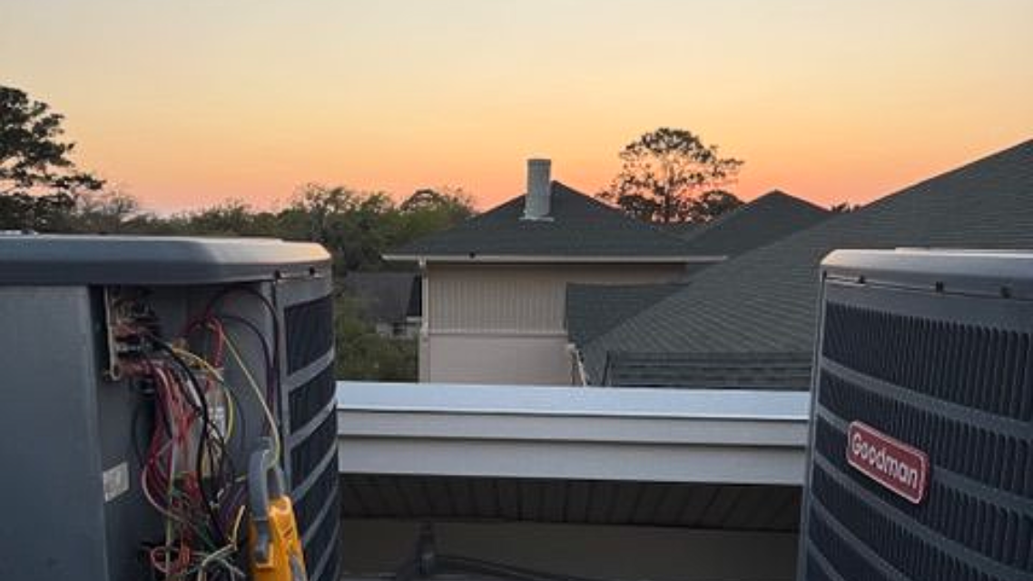 Outdoor HVAC units on a rooftop at sunset, with rooftops and trees in the distance.
