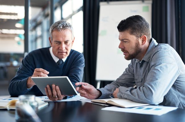 Two coworkers reviewing a tablet and document at a conference table in an office
