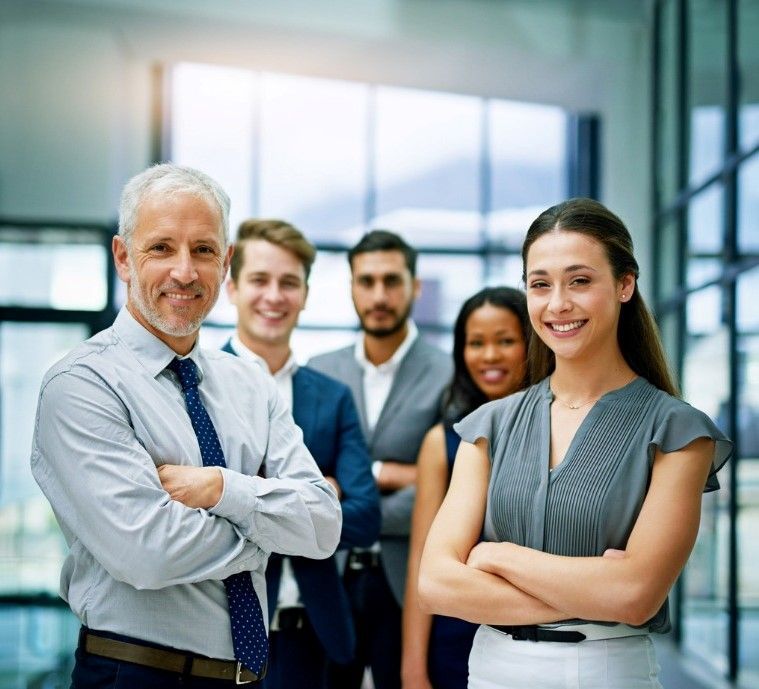 Five office coworkers standing together in a bright modern workspace, arms crossed and smiling