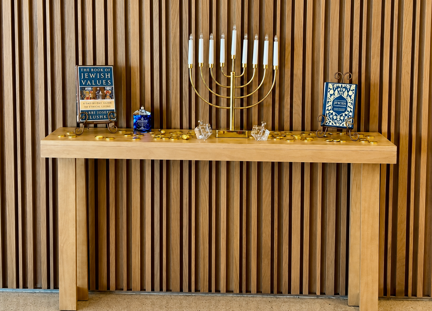 Wooden table with a gold menorah, blue candles, and framed holiday items against a striped wood wall