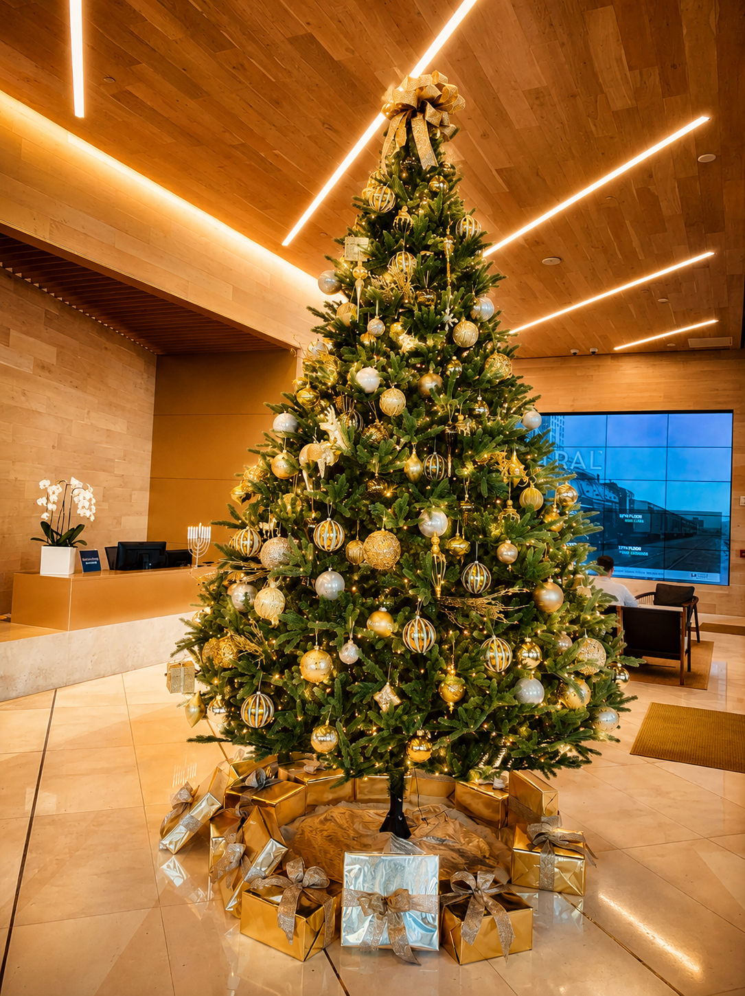 Large decorated Christmas tree in a modern lobby with wrapped gifts underneath