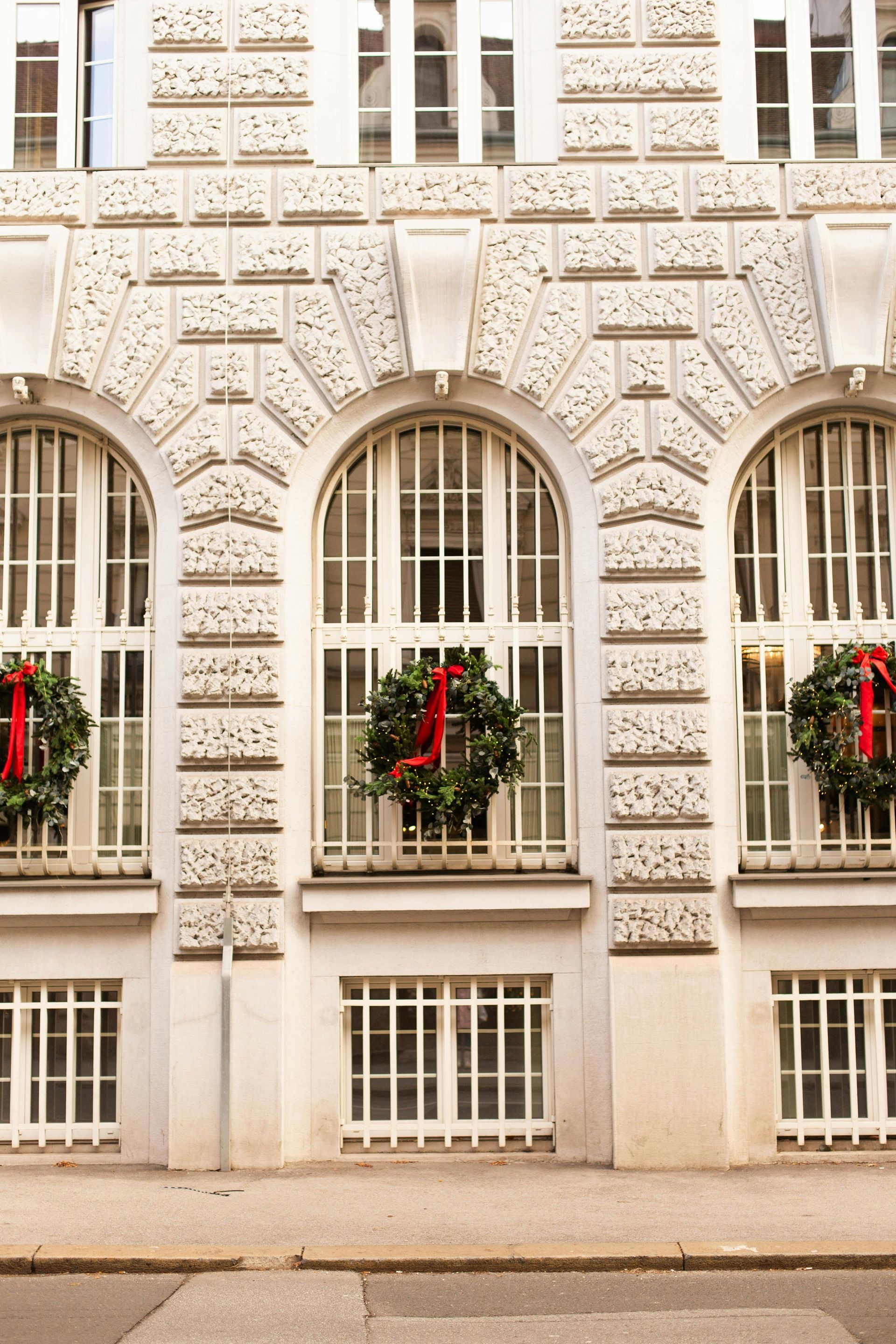 Ornate cream building facade with arched windows and red holiday wreaths behind the glass
