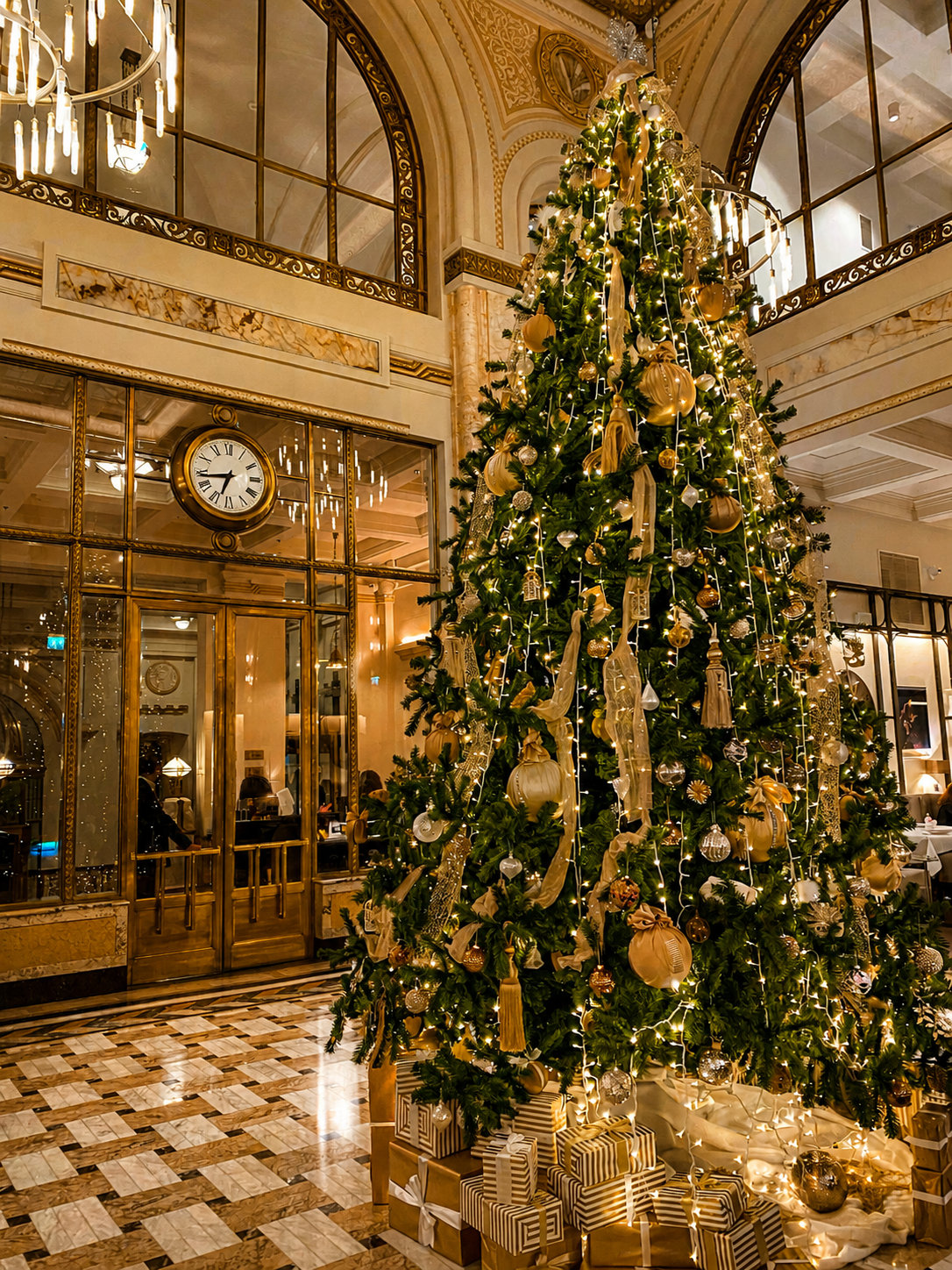 Tall Christmas tree with gold ornaments in an elegant hall with glass doors and a clock