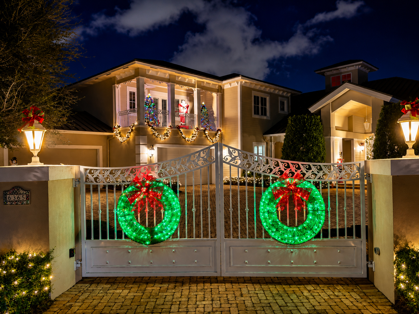 House decorated with glowing Christmas wreaths on a gated driveway at night