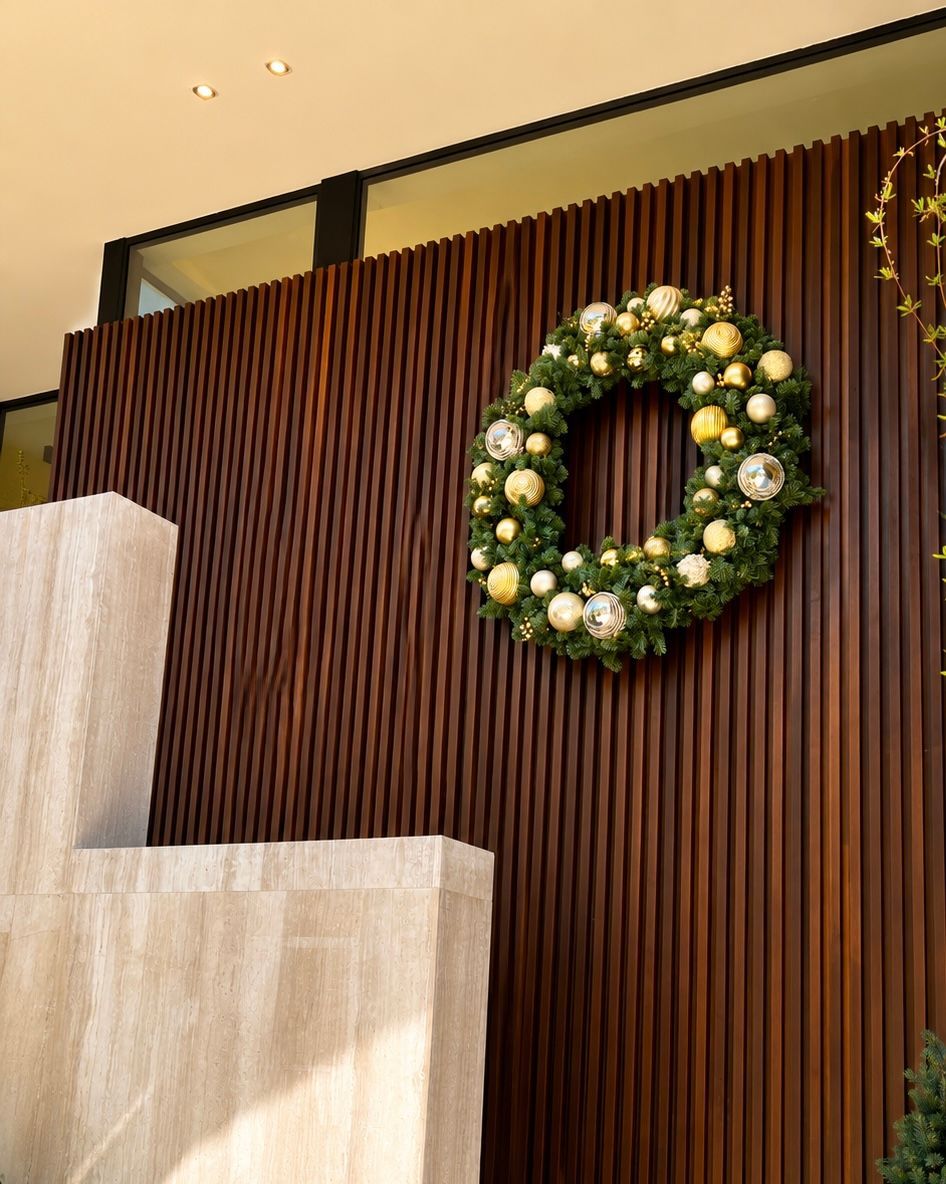 Green floral wreath with white and gold accents on a dark wood-paneled wall indoors.