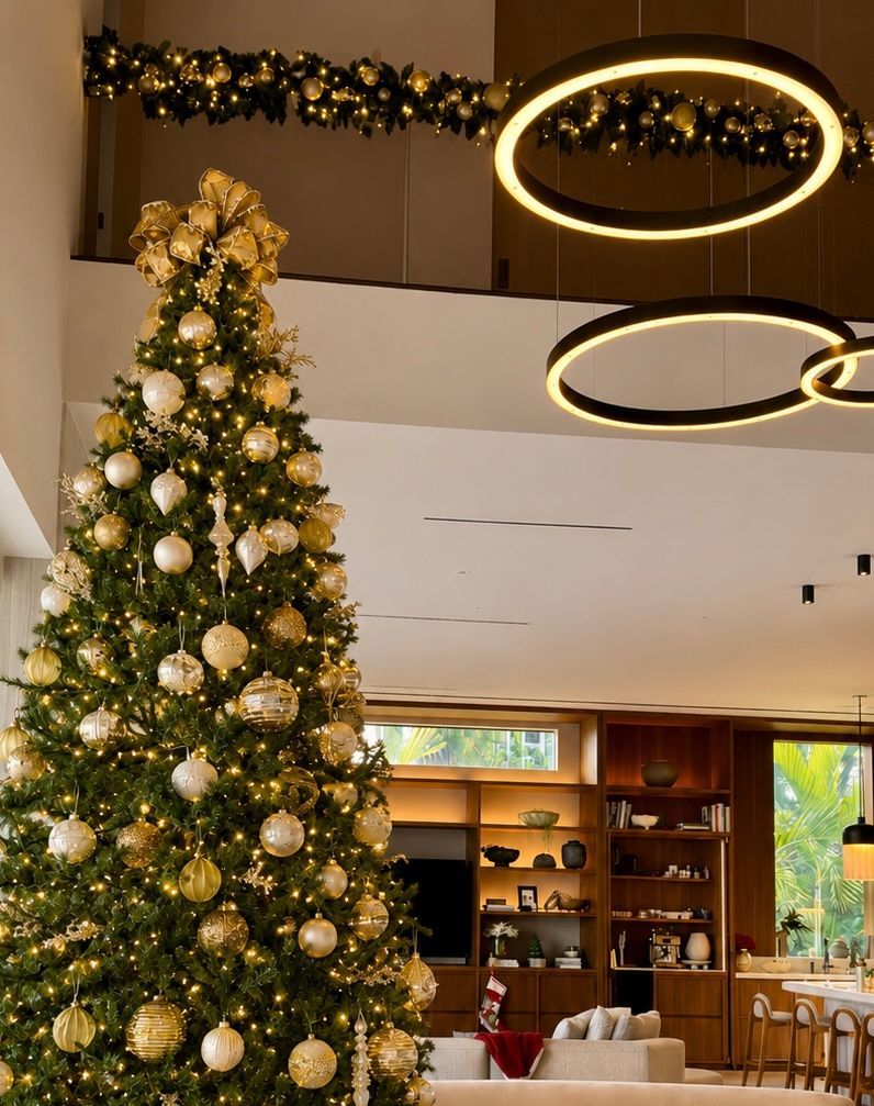 Large decorated Christmas tree in a modern lobby with gold ornaments and circular ceiling lights