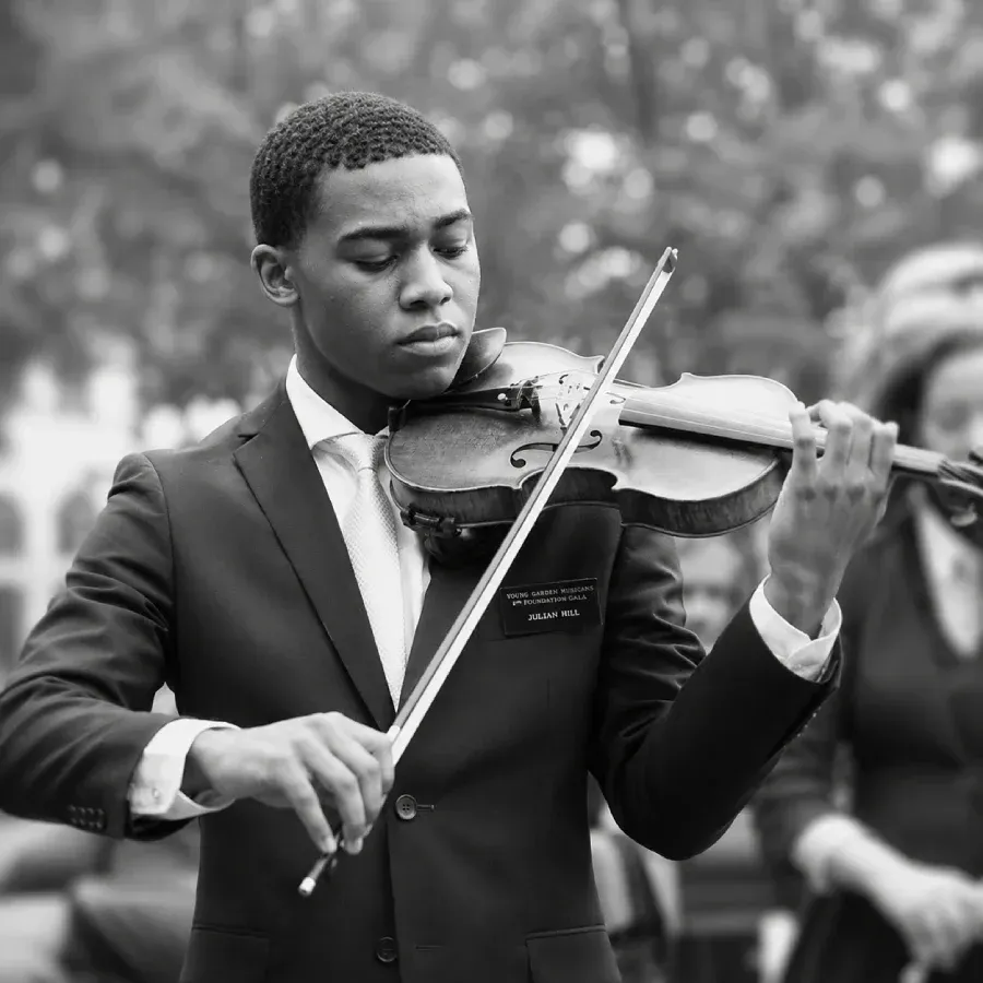 A violinist in a suit plays outdoors, focused on his instrument.