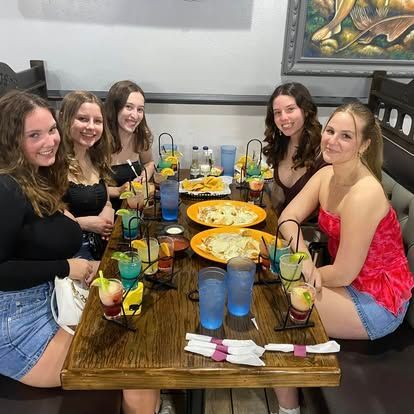 Five young people at a restaurant table with food, drinks, and smiles.
