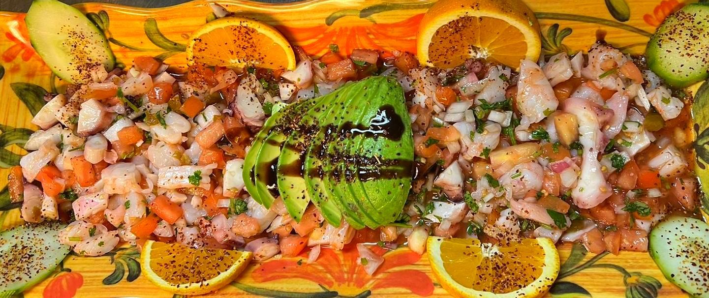 Ceviche dish with shrimp, avocado, orange slices, and cucumber, garnished on a decorated plate.