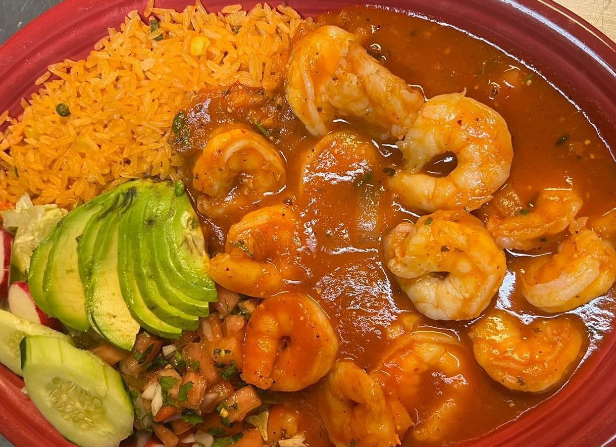Shrimp in red sauce with rice, avocado, and pico de gallo on a red plate.