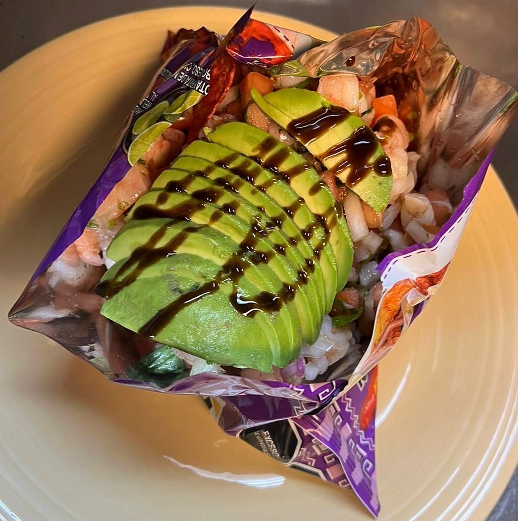 Shrimp ceviche in a chip bag with avocado and balsamic glaze on a yellow plate.