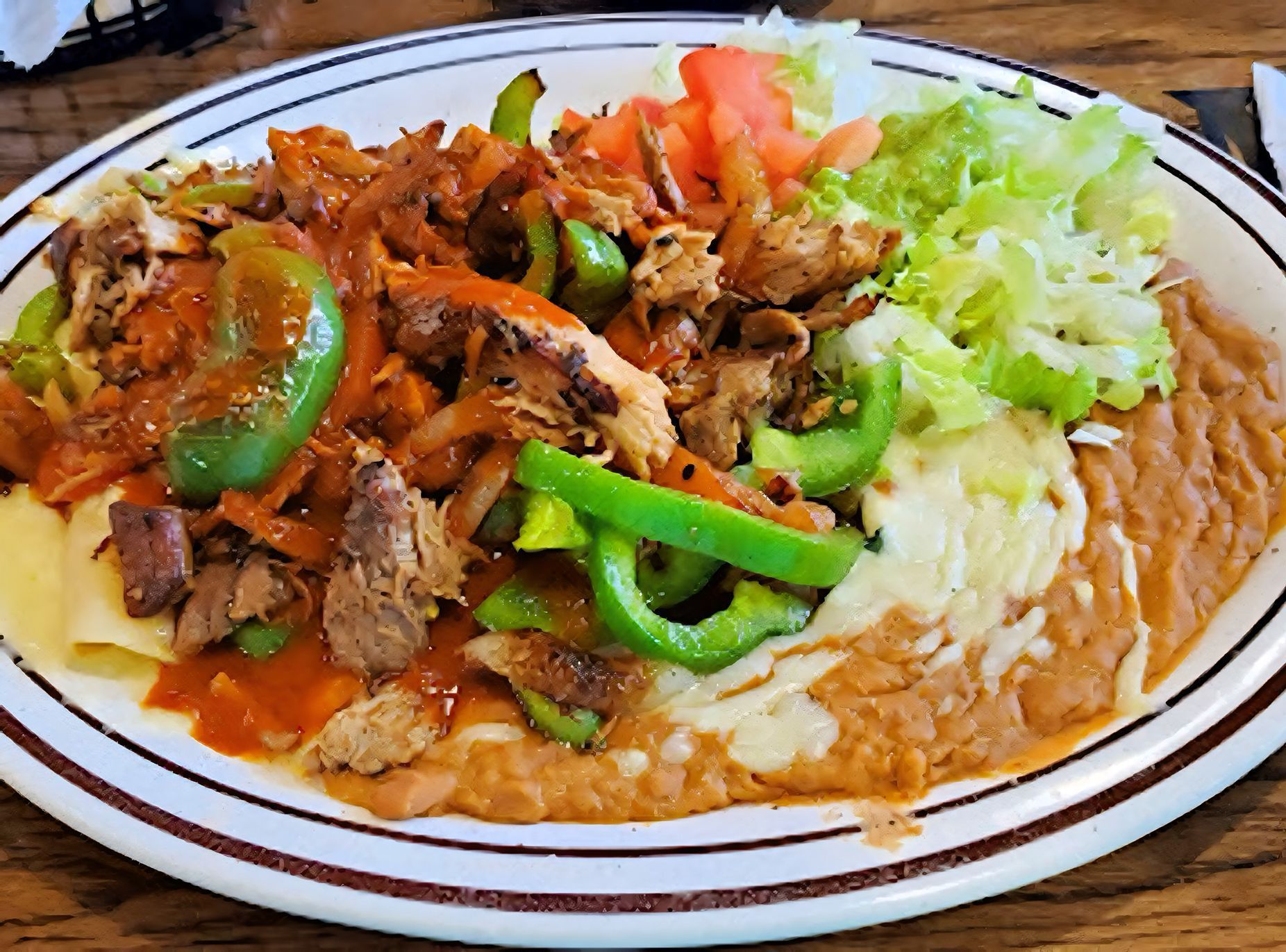 Plate of Mexican food: meat, peppers, beans, lettuce, tomatoes, and cheese.
