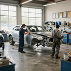 Dos mecánicos trabajando en la carrocería de un coche plateado en un taller de reparación de automóviles con herramientas y certificados en la pared.