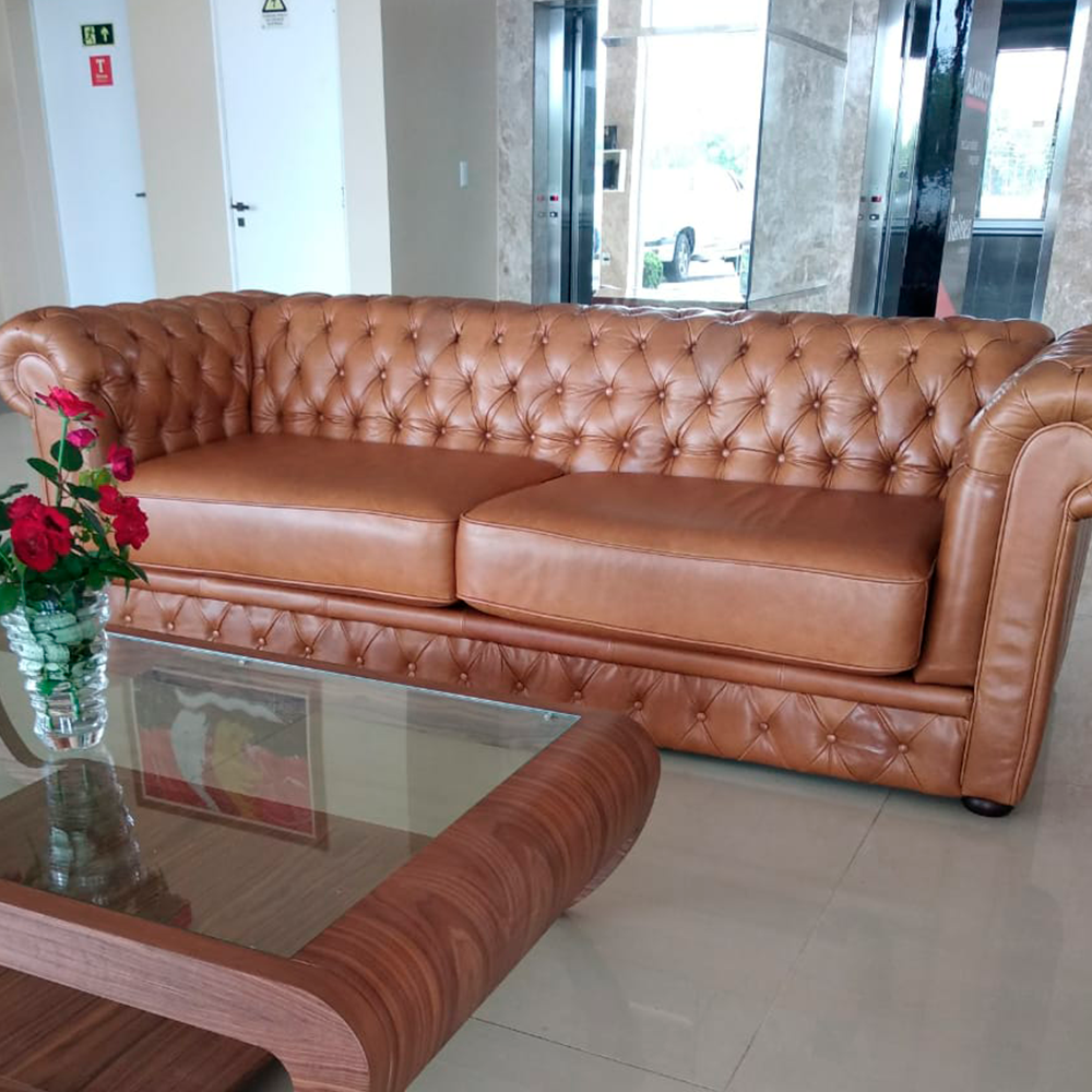 Um sofá de couro marrom está ao lado de uma mesa de centro de vidro.