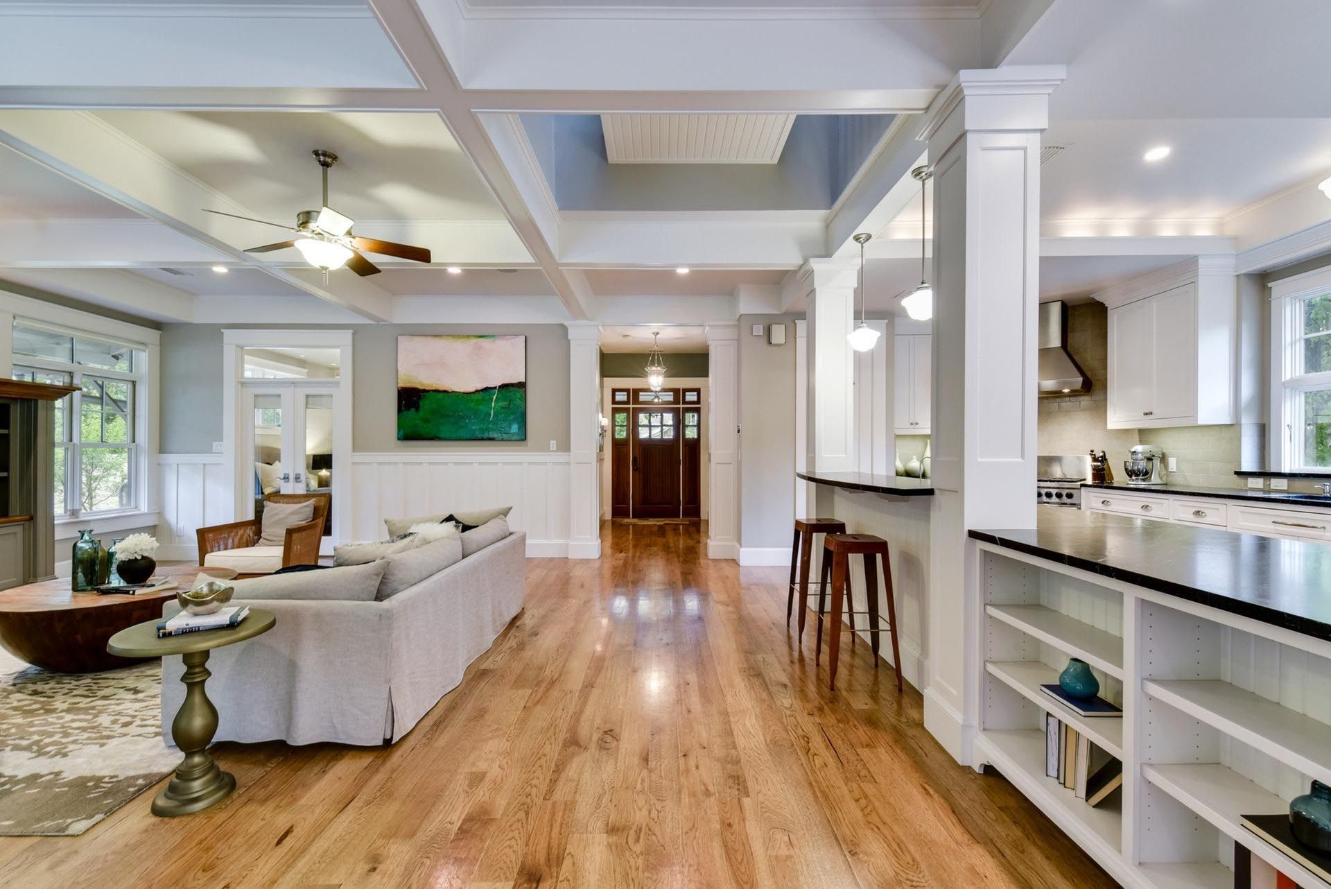 Open-concept living space with hardwood floors, white columns, and a kitchen visible in the background.