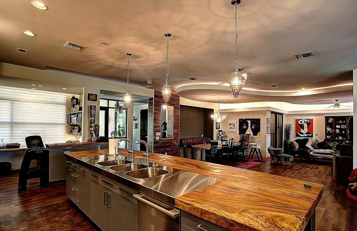 Kitchen with stainless steel island, granite countertop, pendant lights, and living area in the background.