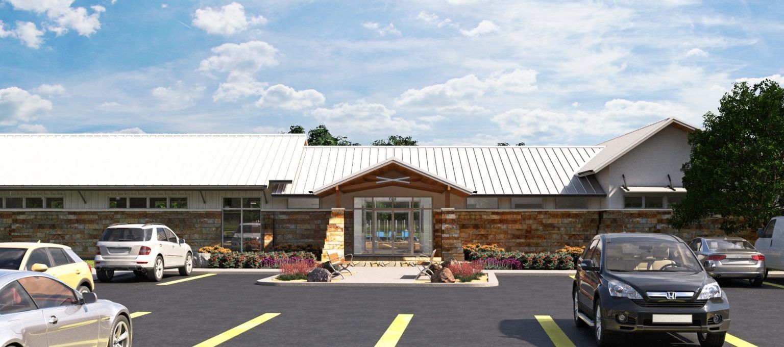 A single-story building with a light-colored roof and a stone facade, featuring a center entrance and a parking lot.