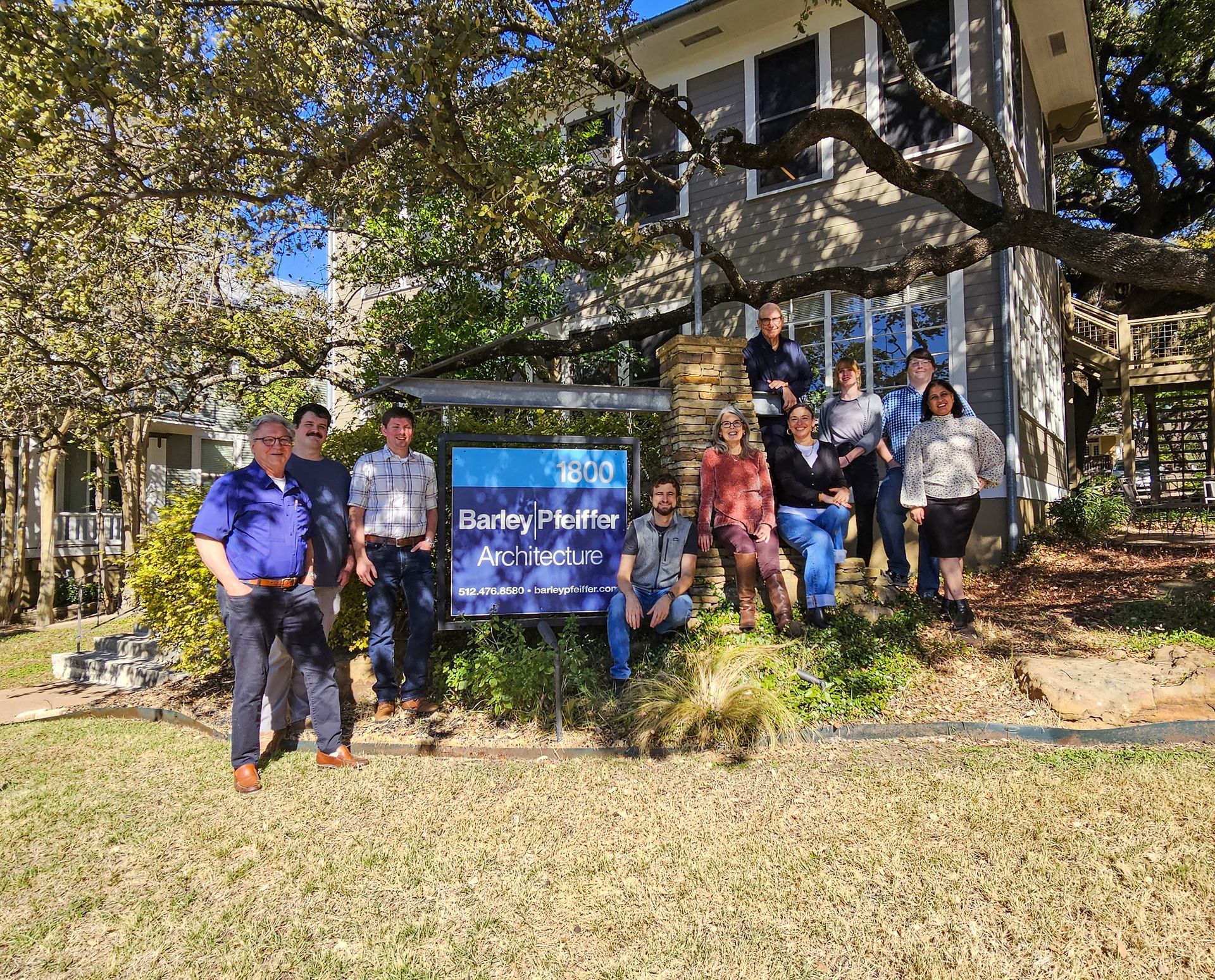 A group of twelve people stands outside in front of a sign for 