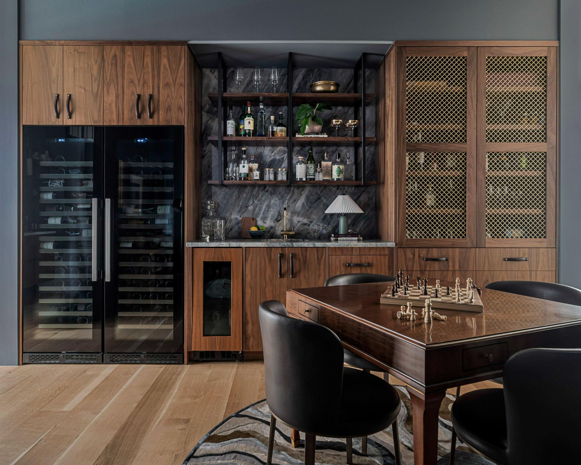 A home bar with wooden cabinetry, wine coolers, shelves, and a chess table.
