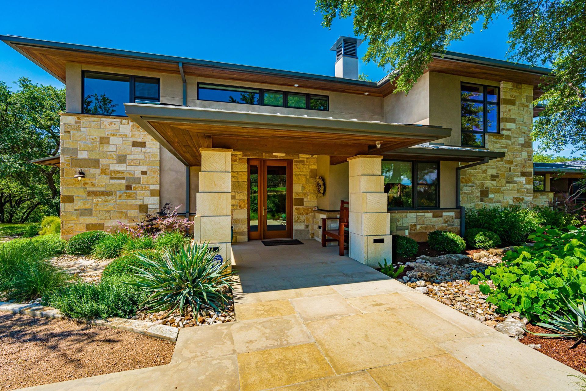 Modern home with tan stone facade, wooden accents, and manicured landscaping.