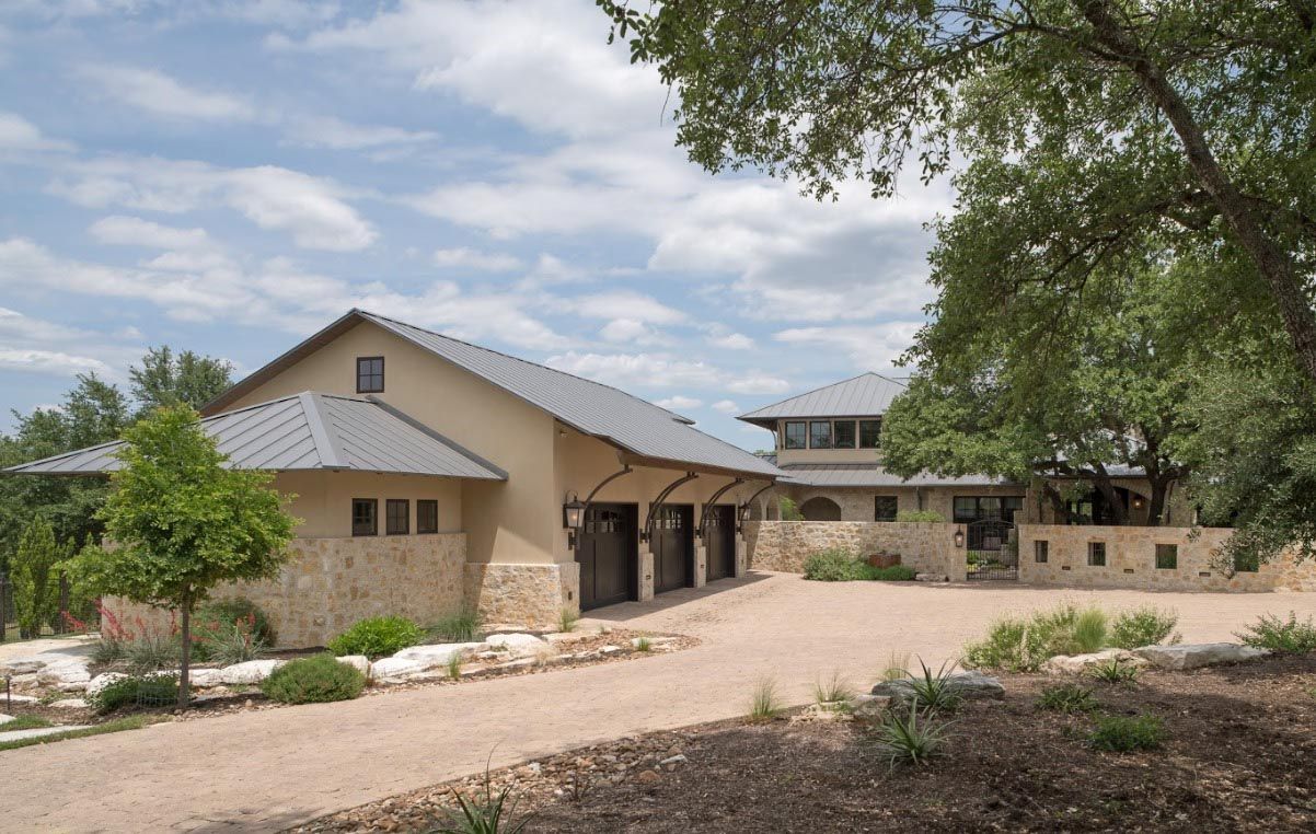 A modern home with a gravel driveway, stone accents, and a gray roof under a partly cloudy sky.