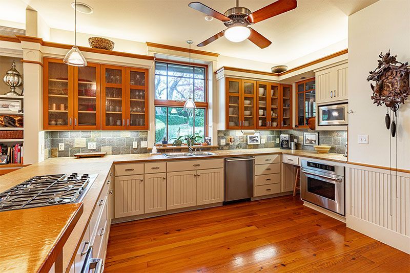 A bright kitchen with wood floors, light-colored cabinets, a stainless steel oven, and upper cabinets with glass fronts.