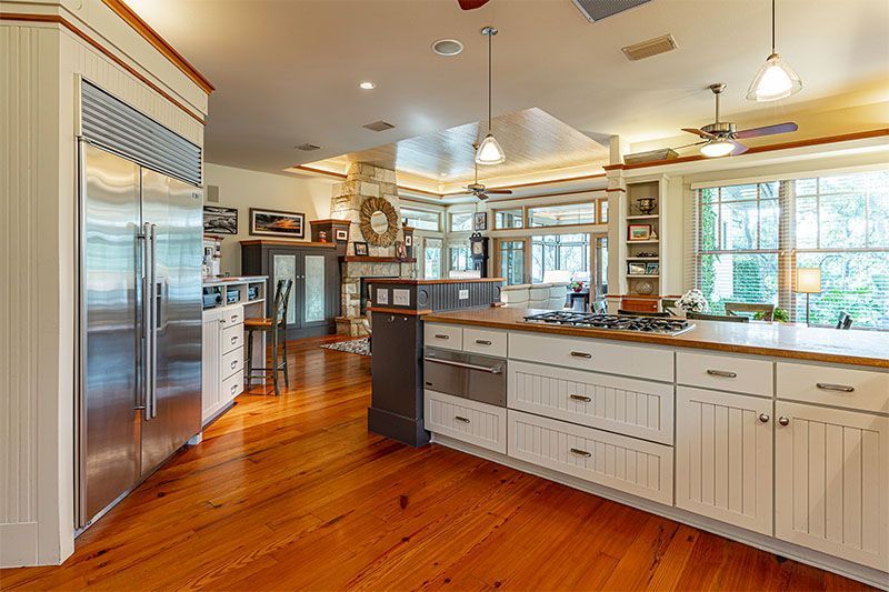 A bright, spacious kitchen featuring a large white island with a stovetop, wood flooring, and a stainless steel fridge.