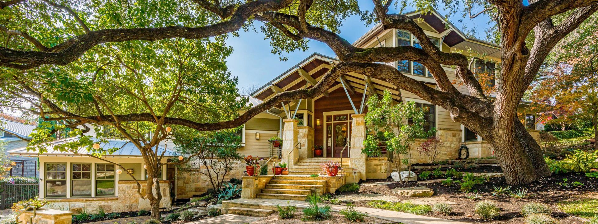 A two-story home with a stone facade, a wooden porch, and a large tree in front.