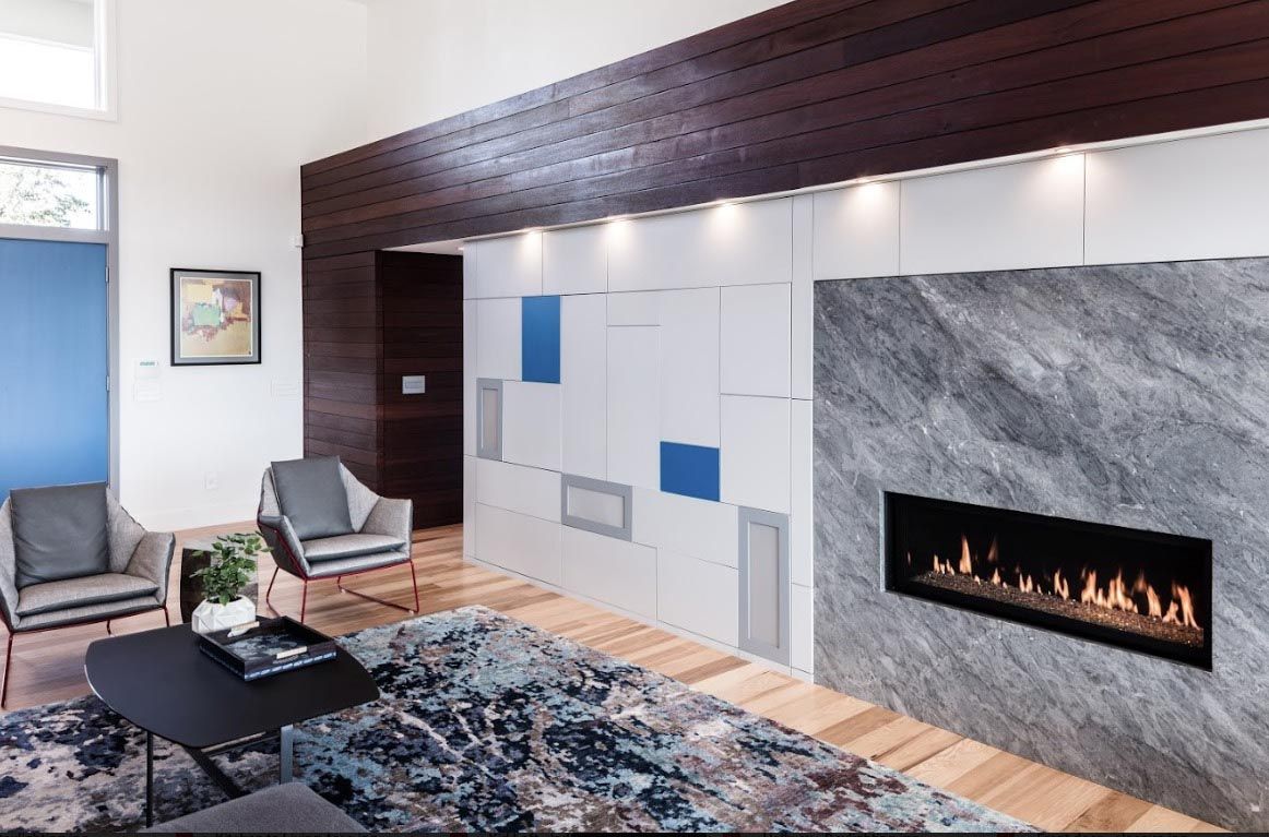 Modern living room with fireplace, wood floors, gray chairs, and blue accents.