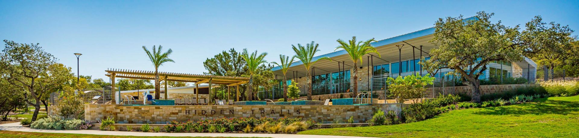 A modern building with large windows and a green lawn under a clear blue sky, surrounded by trees.