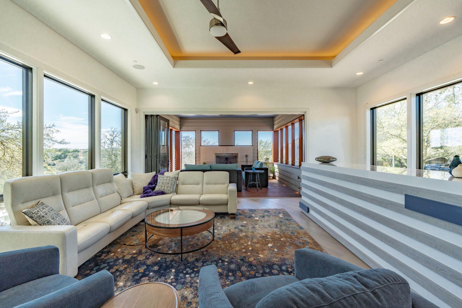 Modern living room with white sectional, blue armchairs, and large windows overlooking the outdoors.