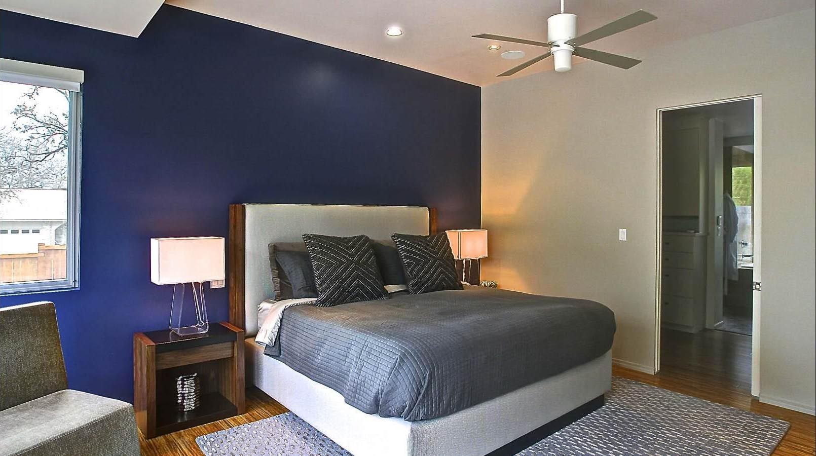 Bedroom with a navy blue accent wall, a gray bed, and wooden floors.