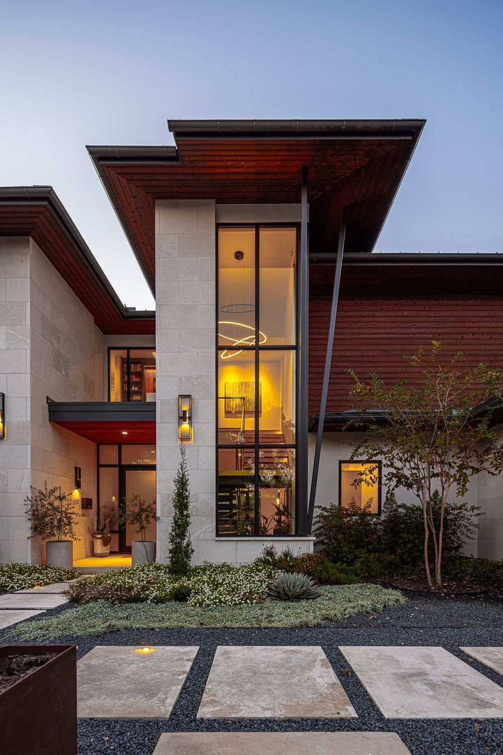 Modern house exterior with stone walls, horizontal wood siding, a tall glass window section, and a landscaped driveway.