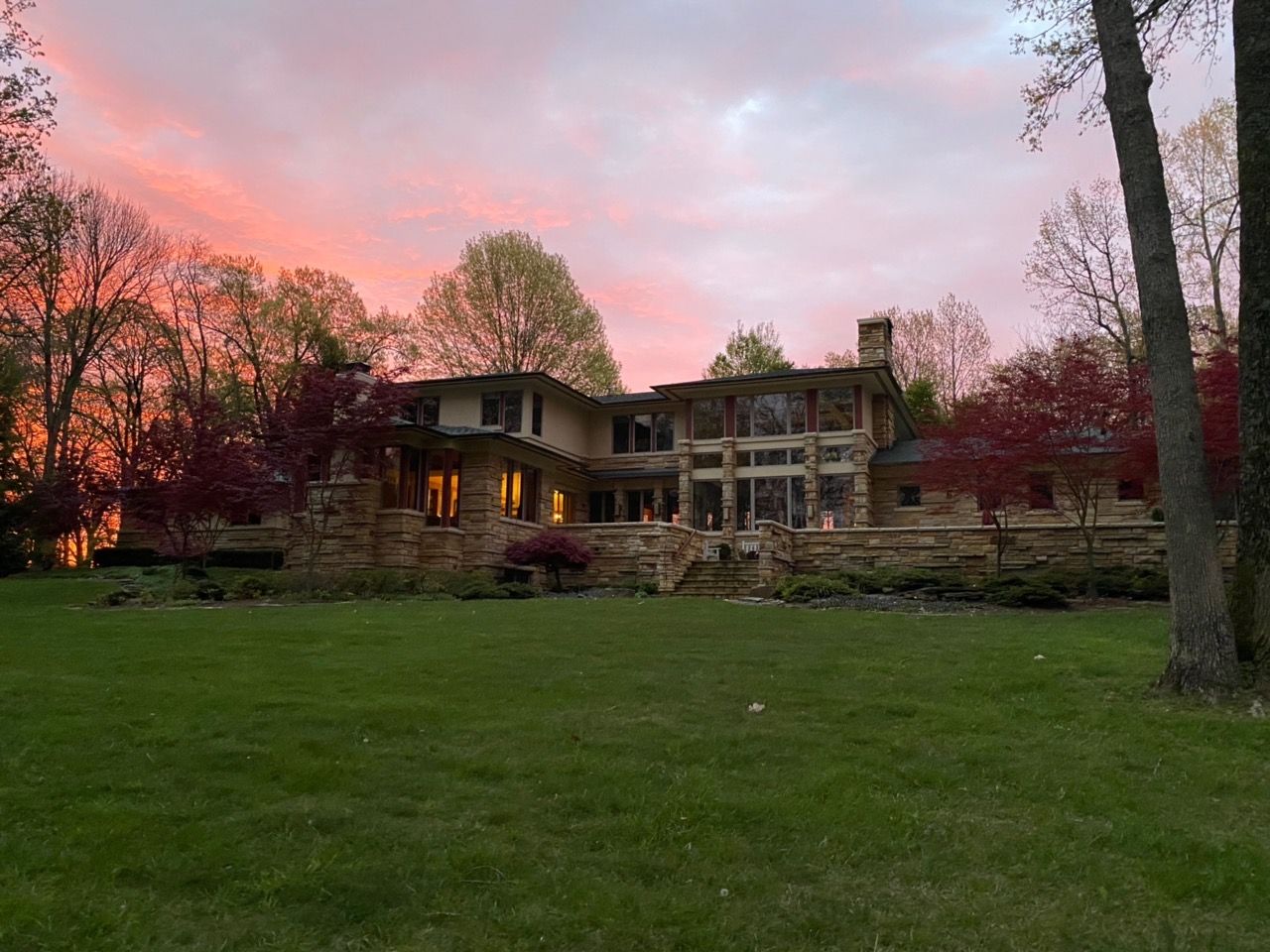 A large house is sitting in the middle of a lush green field at sunset.