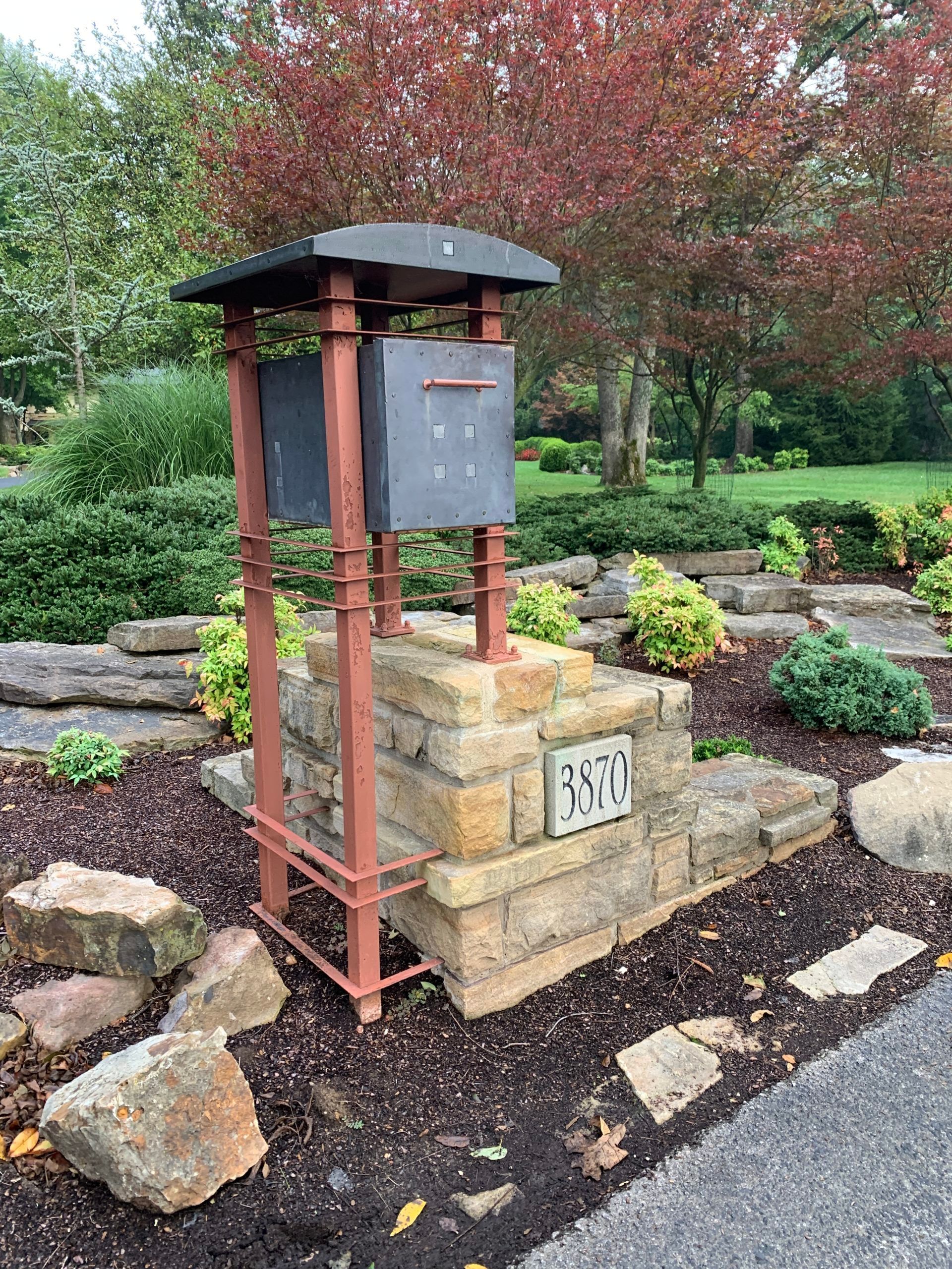 A mailbox is sitting on top of a brick pillar in a garden.