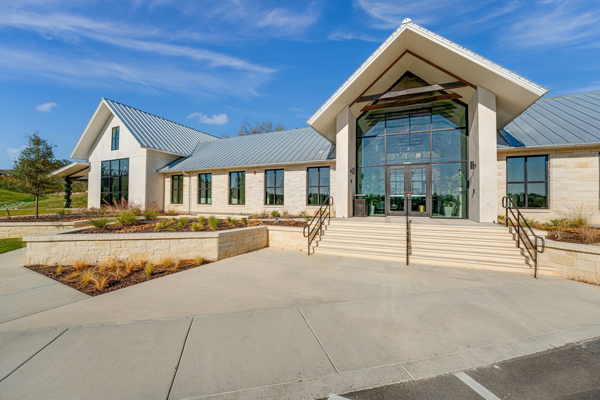 Modern building entrance with glass atrium, stone steps, and landscaped courtyard under a blue sky