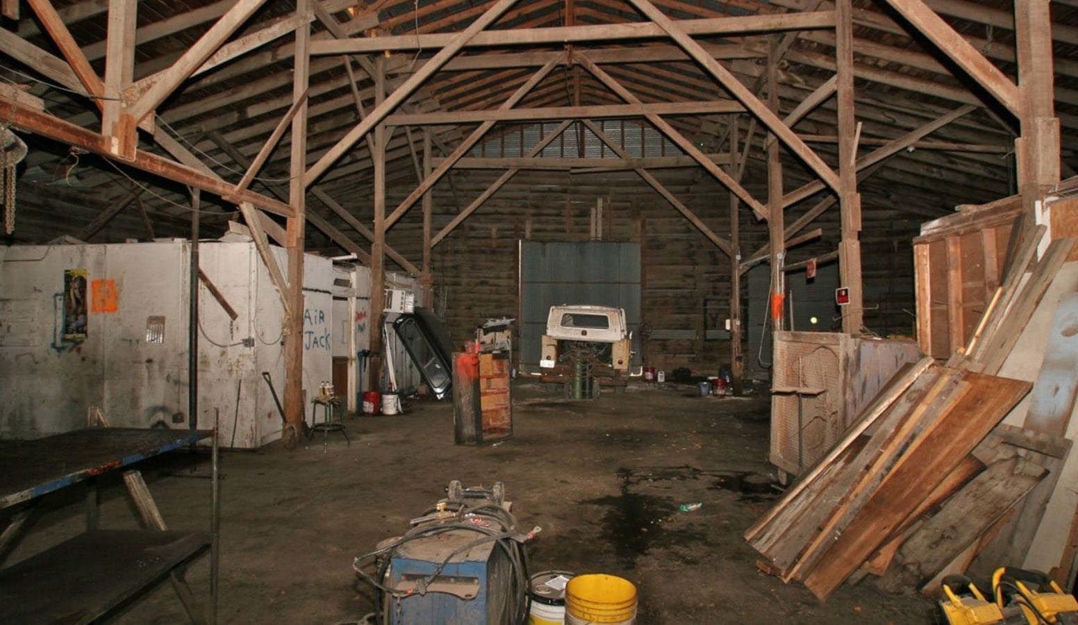 Interior of a weathered barn with wooden beams and various tools, equipment and supplies.
