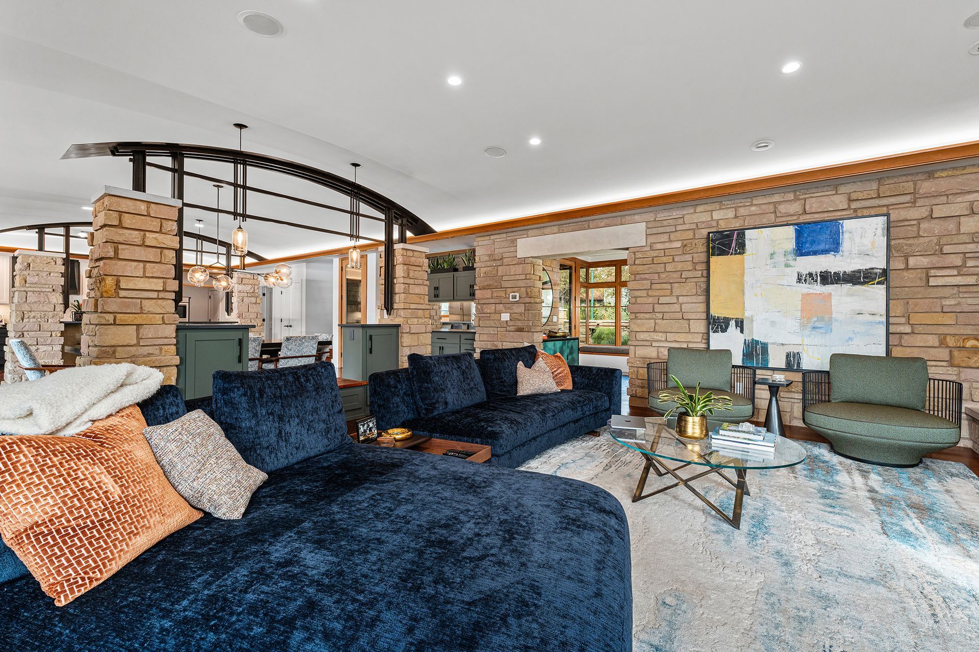 A plush dark blue sectional sofa sits in a living room featuring a stone wall, abstract art, and a geometric coffee table.