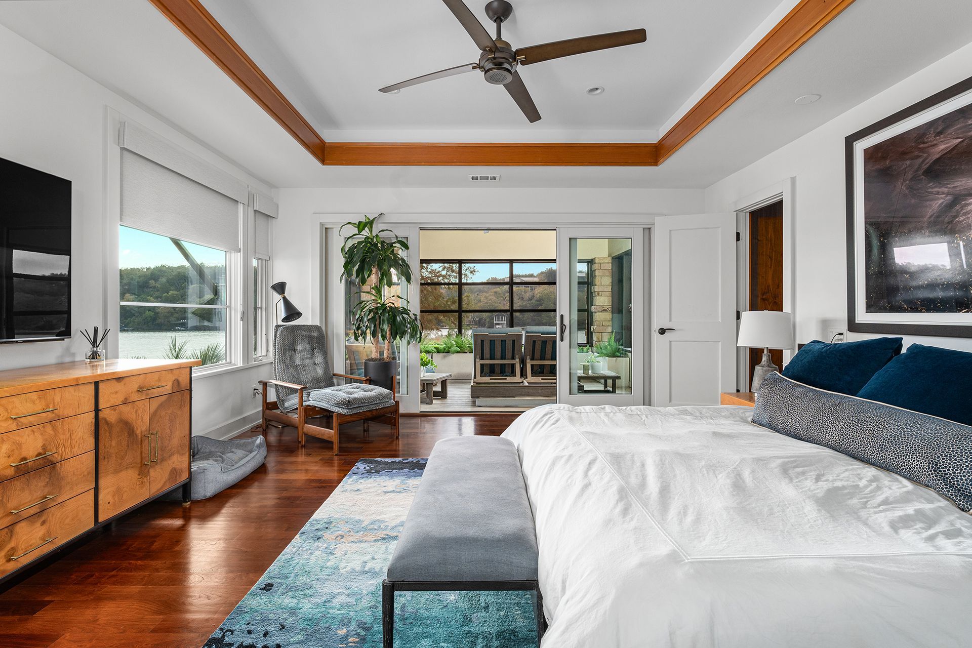 A bright bedroom with a white bed, patterned rug, wood floors, ceiling fan, and sliding doors leading to a patio.