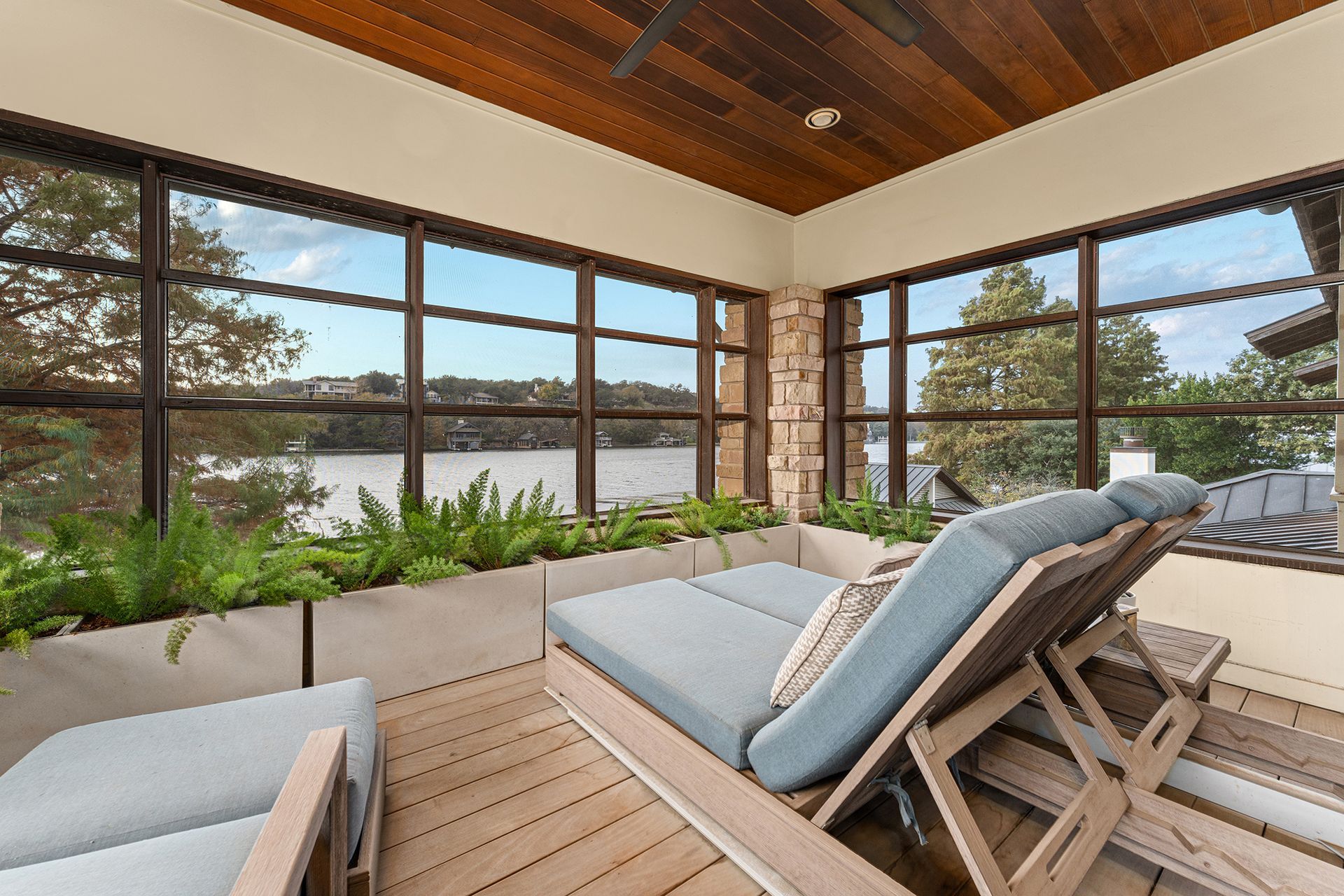 Two light-blue lounge chairs sit on a wood-decked screened porch overlooking a calm lake and treeline.