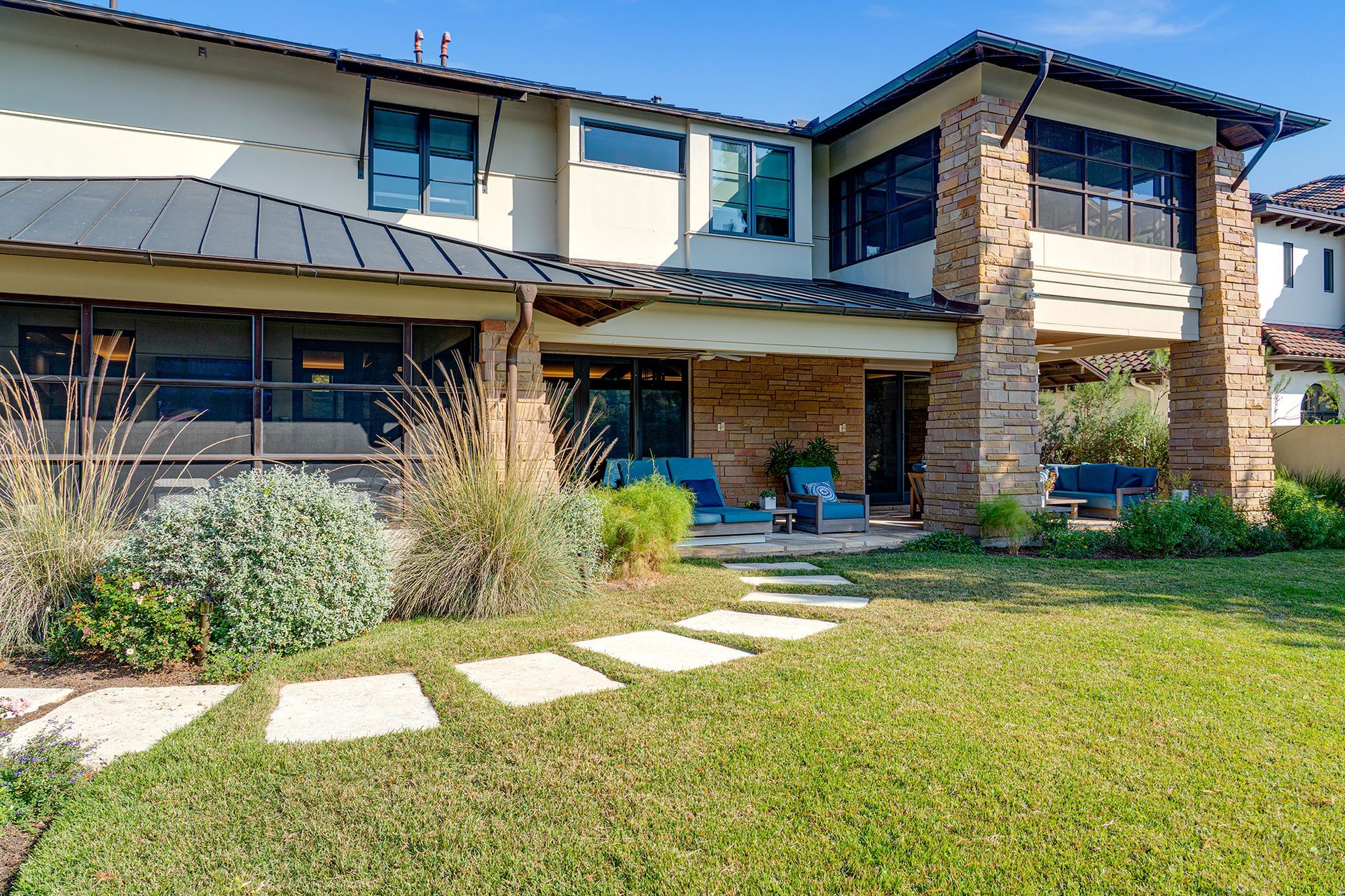 A stone and stucco house with a screened porch and a stone patio, surrounded by a lawn with a stone pathway.