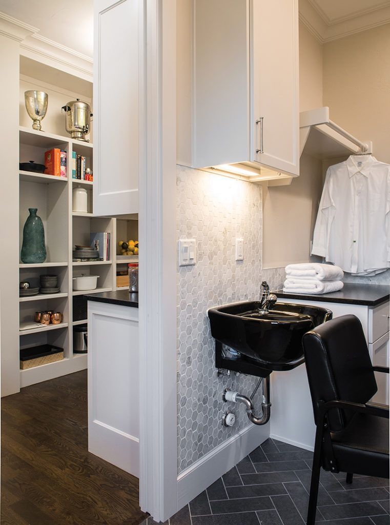 Stylish salon room with shelves, white cabinetry, black sink, and chair on dark wood and tile flooring.