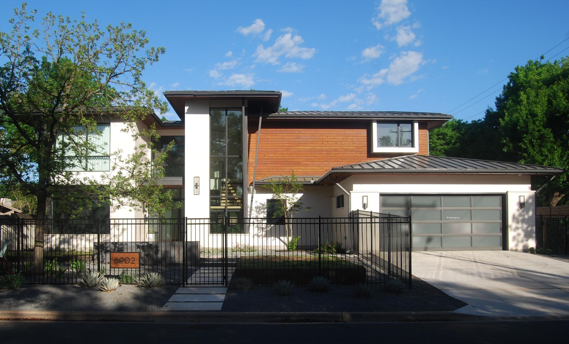 A modern two-story home with white stucco, wood-paneled siding, a large vertical window, and an attached garage.